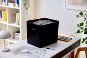 Schwarze Archivbox auf einem Schreibtisch, gefüllt mit Hängemappen, seitliche Perspektive
