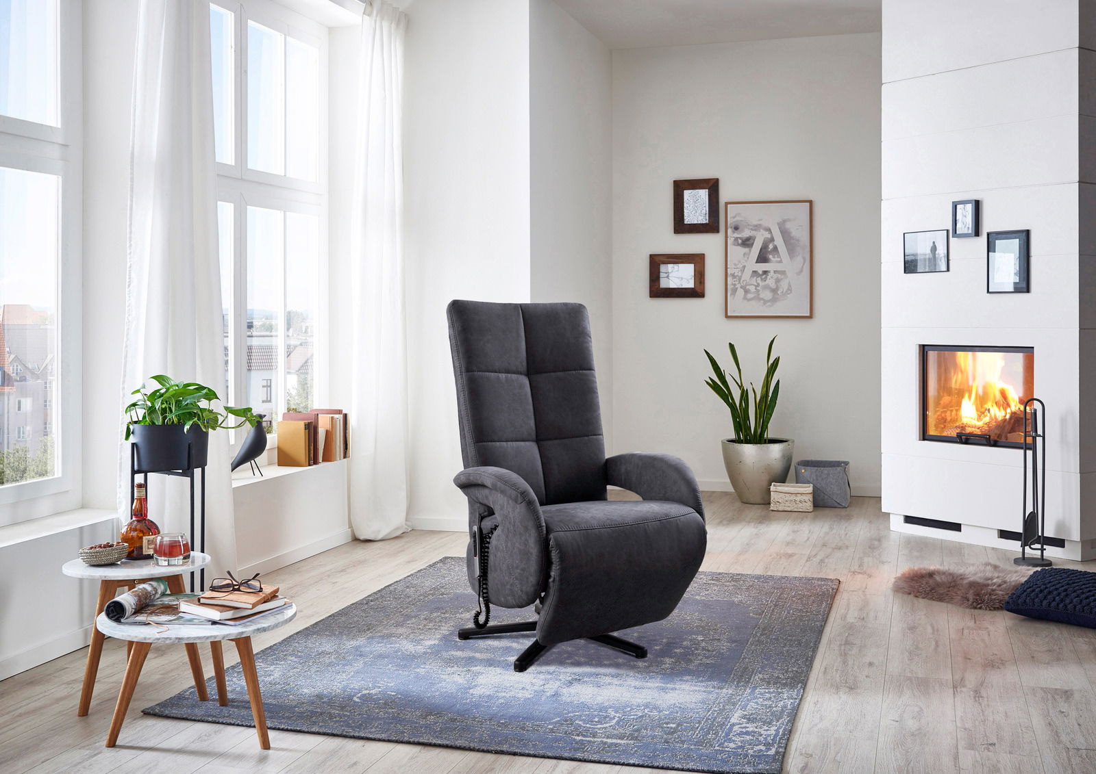 Grauer Sessel in einem modernen Wohnzimmer mit Kamin, Pflanzen und großen Fenstern, seitliche Perspektive.