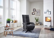 Grauer Sessel in einem modernen Wohnzimmer mit Kamin, Pflanzen und großen Fenstern, seitliche Perspektive.