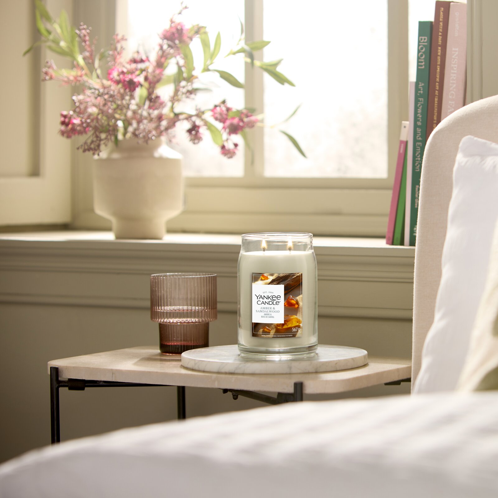 Yankee Candle Signature Duftkerze Amber & Sandalwood im großen Glas mit zwei brennenden Dochten, frontal auf einem Beistelltisch in einem hellen Wohnambiente präsentiert