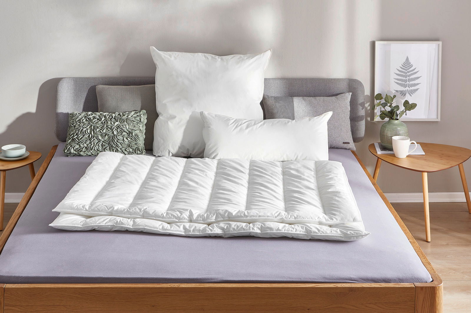 Vegan Dream Solobett 135x200 in einem modernen Schlafzimmer, frontal fotografiert, mit weißen Kissen und Decke, umgeben von einem Nachttisch mit Pflanze und Tasse.