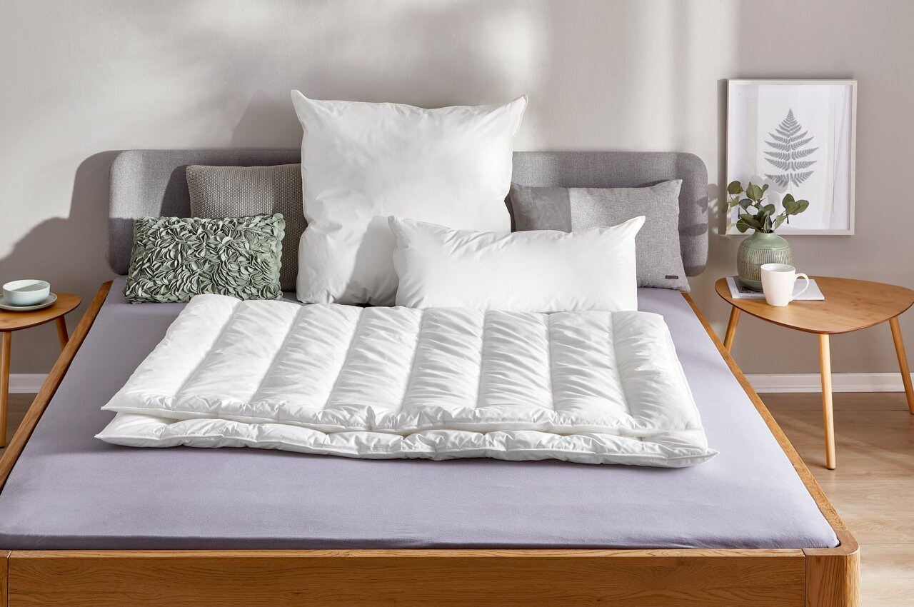 Vegan Dream Solobett 135x200 in einem modernen Schlafzimmer, frontal fotografiert, mit weißen Kissen und Decke, umgeben von einem Nachttisch mit Pflanze und Tasse.