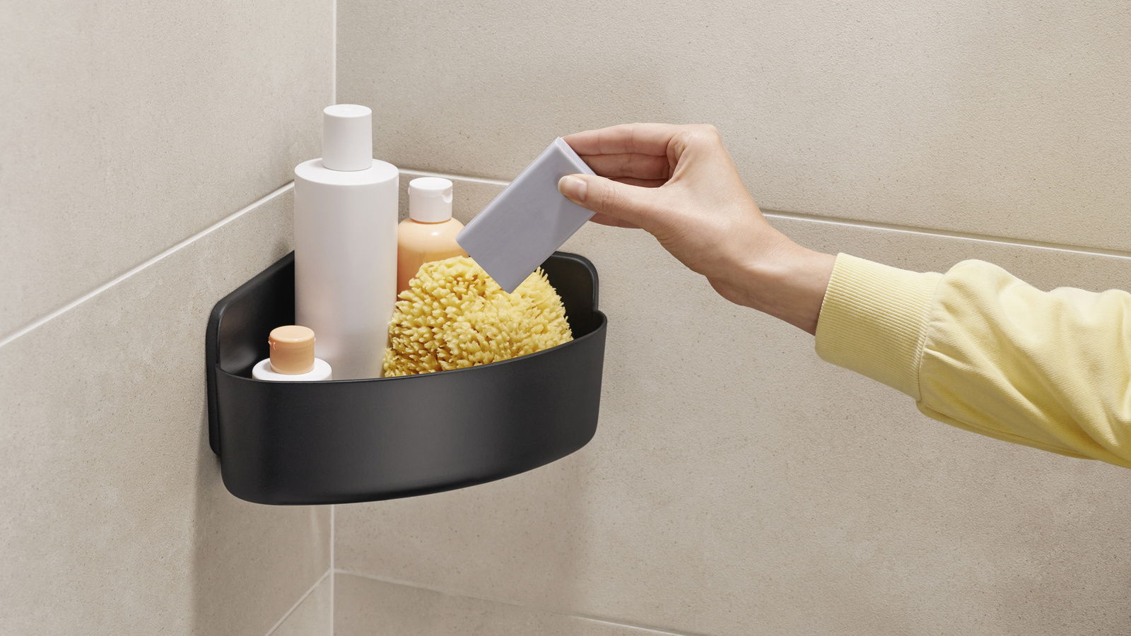 Eckduschkorb in schwarzer Farbe, montiert in einer Duschkabine, gefüllt mit Pflegeprodukten und einem Schwamm, seitliche Perspektive.