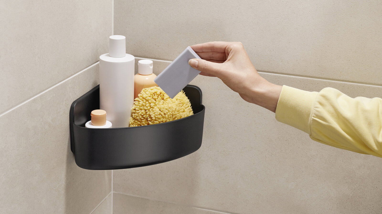Tesa Duschkorb LAVAA Eckduschkorb in schwarzer Farbe, montiert in einer Duschkabine, gefüllt mit Pflegeprodukten und einem Schwamm, seitliche Perspektive.