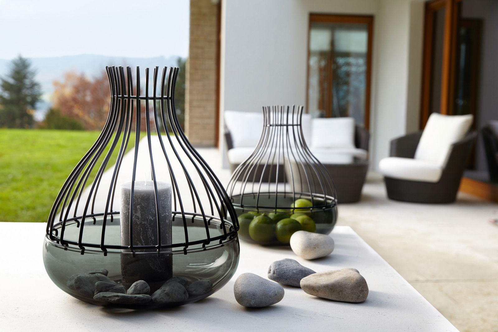 Dekoschale Giardino 25cm aus Glas und Metall mit Kerze und Steinen, im Vordergrund auf einem Tisch in einem modernen Außenbereich platziert, seitliche Perspektive