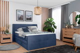 Boxspringbett 120 in einem modernen Schlafzimmer, seitliche Perspektive, mit blauer Polsterung und dekorativen Kissen.