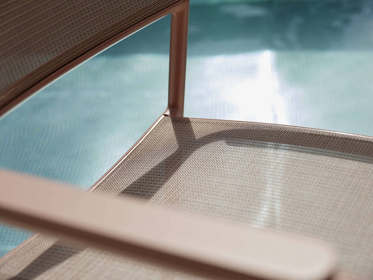 Nahaufnahme eines Stapelsessels mit Metallrahmen und Netzbespannung, im Hintergrund ein Pool.