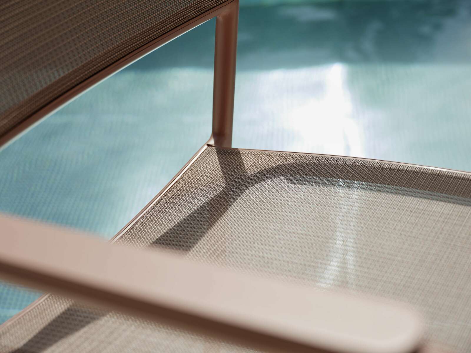 Nahaufnahme eines Stapelsessels mit Metallrahmen und Netzbespannung, im Hintergrund ein Pool.