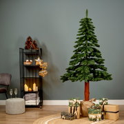 Künstlicher Weihnachtsbaum Tora Kiefer, 180 cm hoch, in einem gemütlich dekorierten Raum mit Geschenken und Lichtern, seitliche Perspektive.
