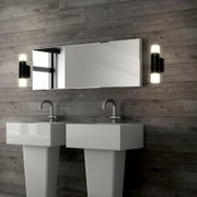 Modernes Badezimmer mit rechteckigem Wandspiegel zwischen zwei schwarzen Wandleuchten, darunter zwei weiße Standwaschbecken; Ansicht frontal auf Augenhöhe.