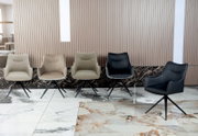 Vijf moderne fauteuils in verschillende kleuren, gezien vanaf de voorkant, op een marmeren vloer voor een geribbelde muur.