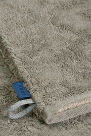 Nahaufnahme eines grauen Waschhandschuhs mit einer blauen Schlaufe und einem Etikett, liegend auf einer flauschigen Oberfläche.