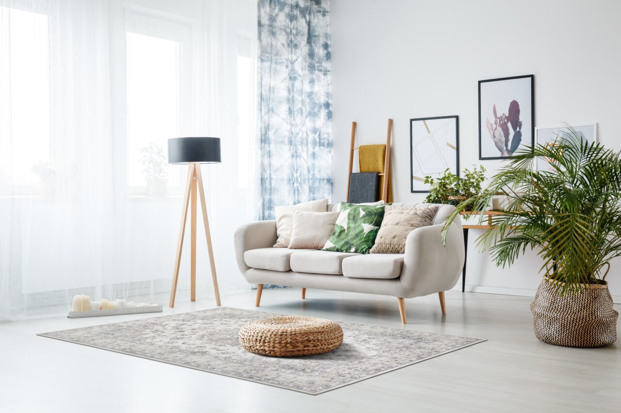 Luxor Living Teppich-Serie PRIMA in einem modernen Wohnzimmer mit Sofa, Pflanzen und Dekorationen, aus der Perspektive von vorne.