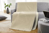 Beige Jacquard-Decke mit der Aufschrift 'MEIN PLATZ!' auf einem grauen Sofa drapiert, seitliche Perspektive.