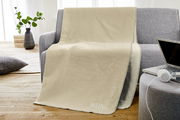 Beige Jacquard-Decke mit der Aufschrift 'MEIN PLATZ!' auf einem grauen Sofa drapiert, seitliche Perspektive.