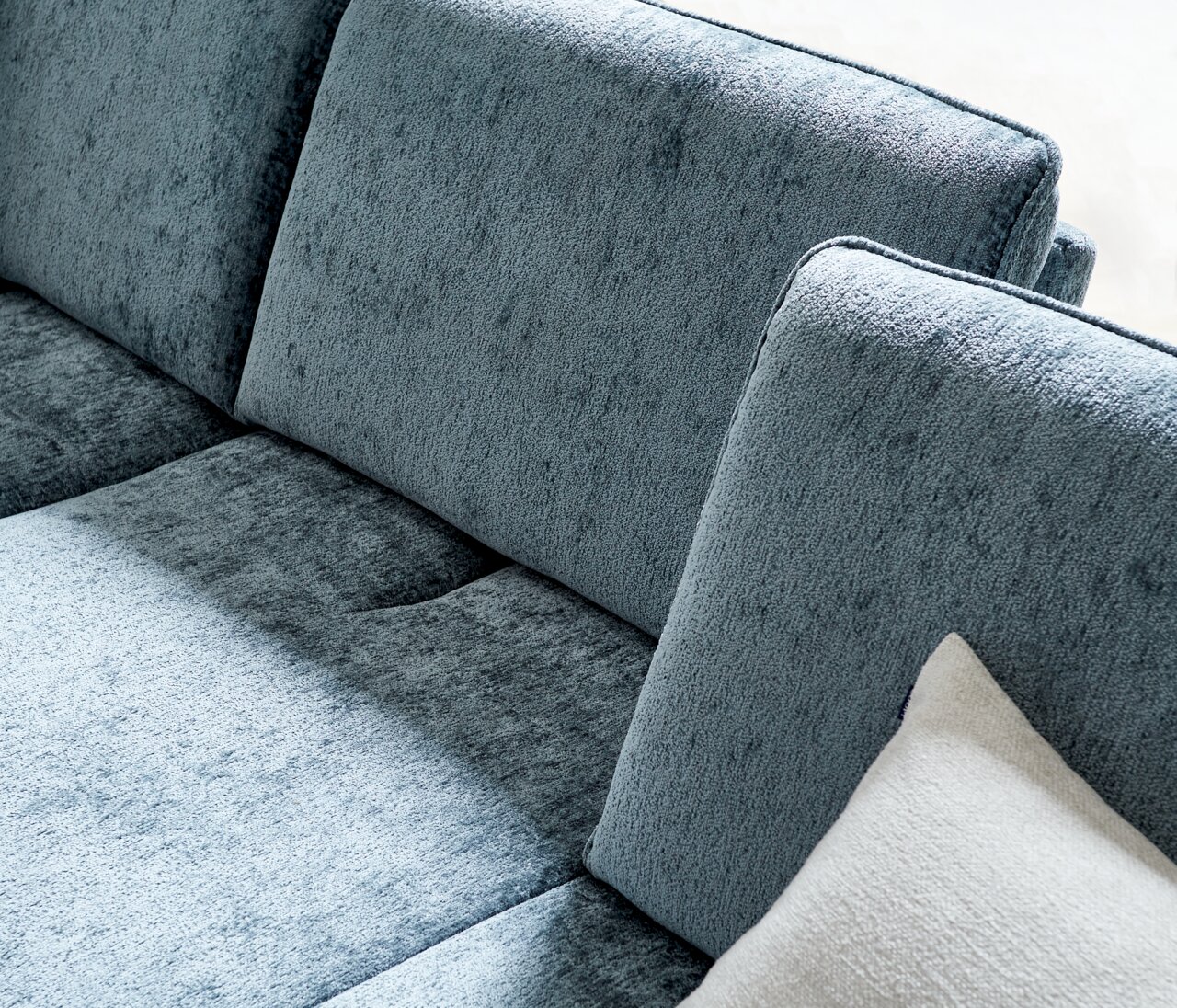 Nahaufnahme einer blauen Longchairkombination mit weicher Textur und einem weißen Kissen, seitliche Perspektive.