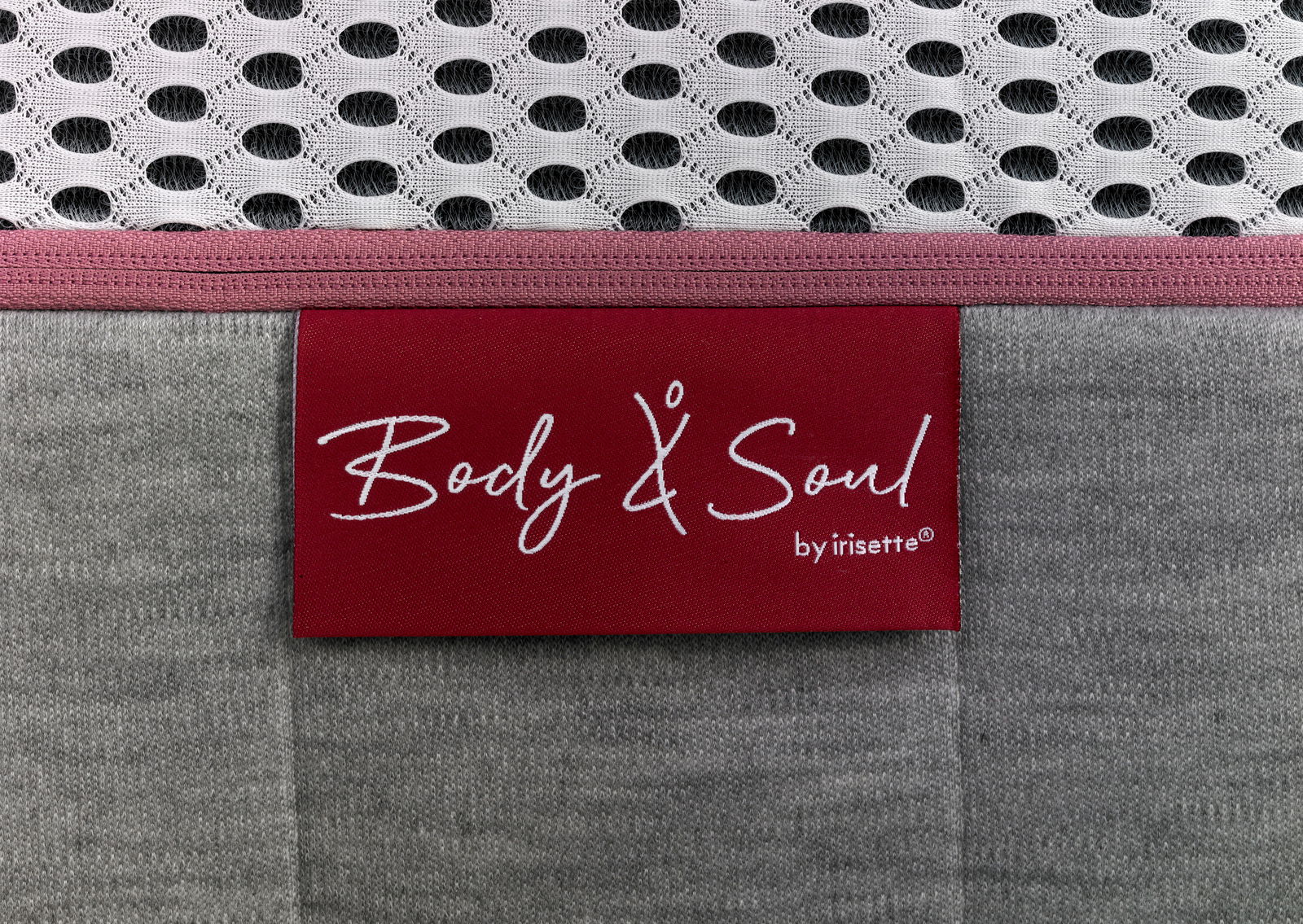 Nahaufnahme einer Matratze mit grauem Stoff und einem roten Etikett mit der Aufschrift 'Body & Soul by irisette'.