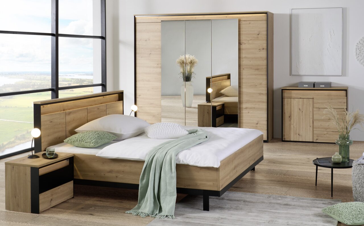 Moderne Schlafzimmermöbel in Holzoptik, bestehend aus einem Bett, Nachttisch, Kleiderschrank mit Spiegel und Kommode, aus der Perspektive eines hellen, geräumigen Zimmers mit großem Fenster.