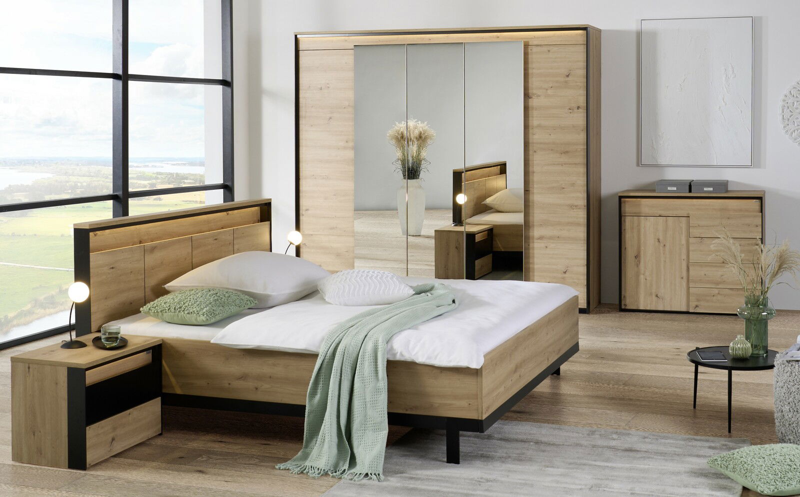 Voleo Kommode Moderne Schlafzimmermöbel in Holzoptik, bestehend aus einem Bett, Nachttisch, Kleiderschrank mit Spiegel und Kommode, aus der Perspektive eines hellen, geräumigen Zimmers mit großem Fenster.