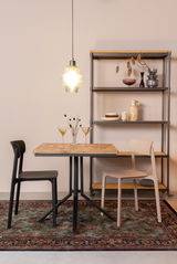 Zwei moderne Stühle in Schwarz und Beige an einem Holztisch, mit einer Hängelampe und einem Regal im Hintergrund, aus seitlicher Perspektive.