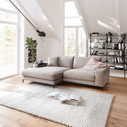 Beige Longchairkombination in einem modernen Wohnzimmer mit schrägen Decken, einem großen Fenster, einem Bücherregal und einem Teppich. Perspektive von vorne links.