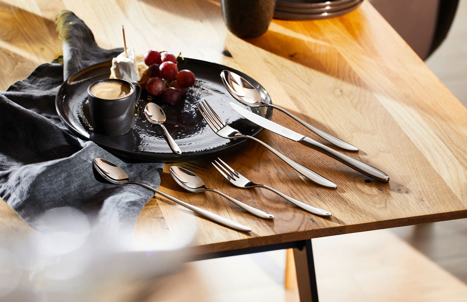 ZWILLING Besteck Beverly 42-tlg. Elegantes Besteckset Beverly 42-tlg. auf einem Holztisch, mit einem Teller, einer Tasse und Trauben, aus der Vogelperspektive.