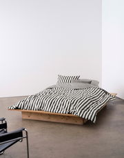 Bett mit gestreifter Bettwäsche in Schwarz-Weiß, auf einem niedrigen Holzrahmen, seitliche Perspektive