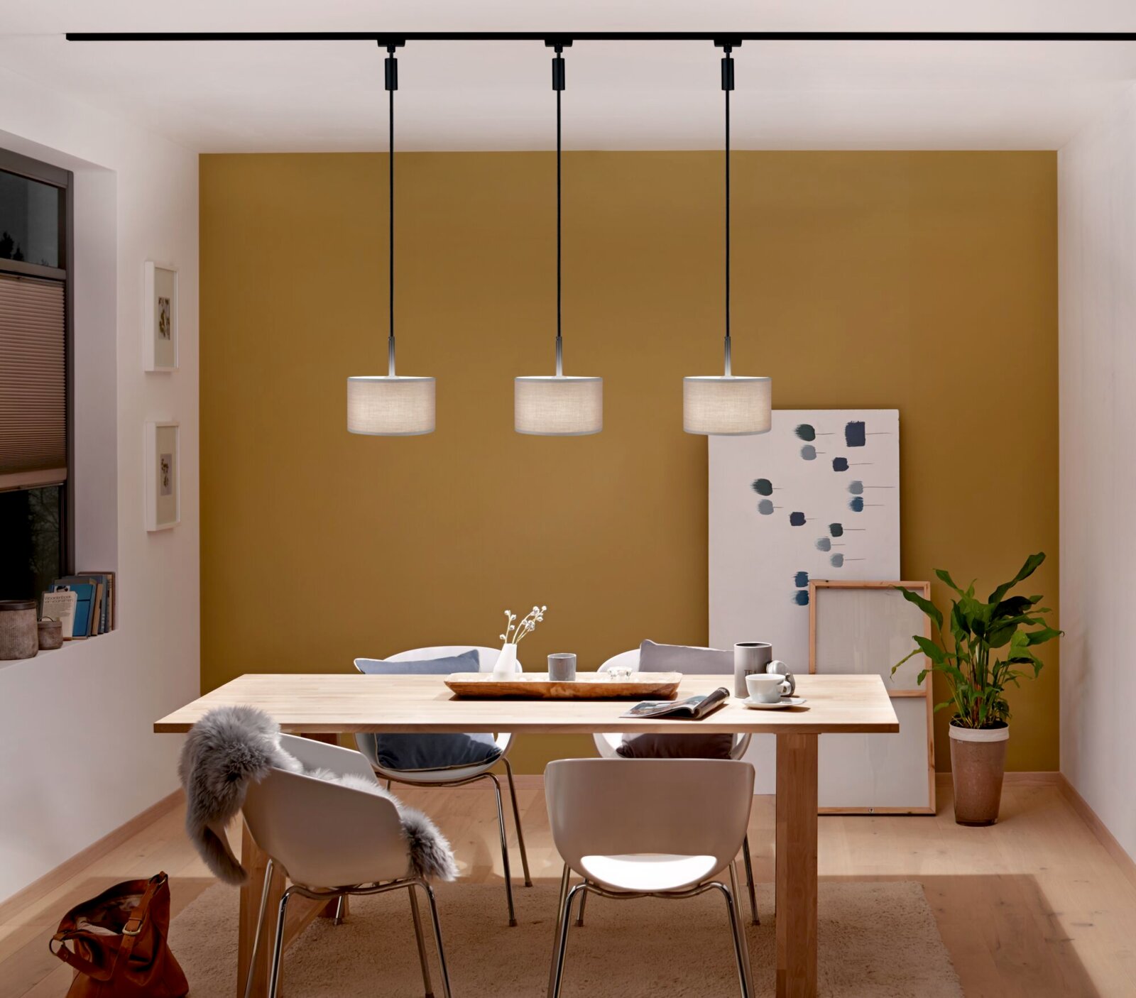 Drei moderne Pendelleuchten in einem Esszimmer, frontal betrachtet, mit einem Holztisch und weißen Stühlen darunter.