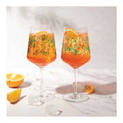 Twee elegante wijnglazen met een tropisch bloemenpatroon, gevuld met een oranje drankje en schijfjes sinaasappel, op een marmeren oppervlak met ijsblokjes en schijfjes sinaasappel op de voorgrond, zijaanzicht.