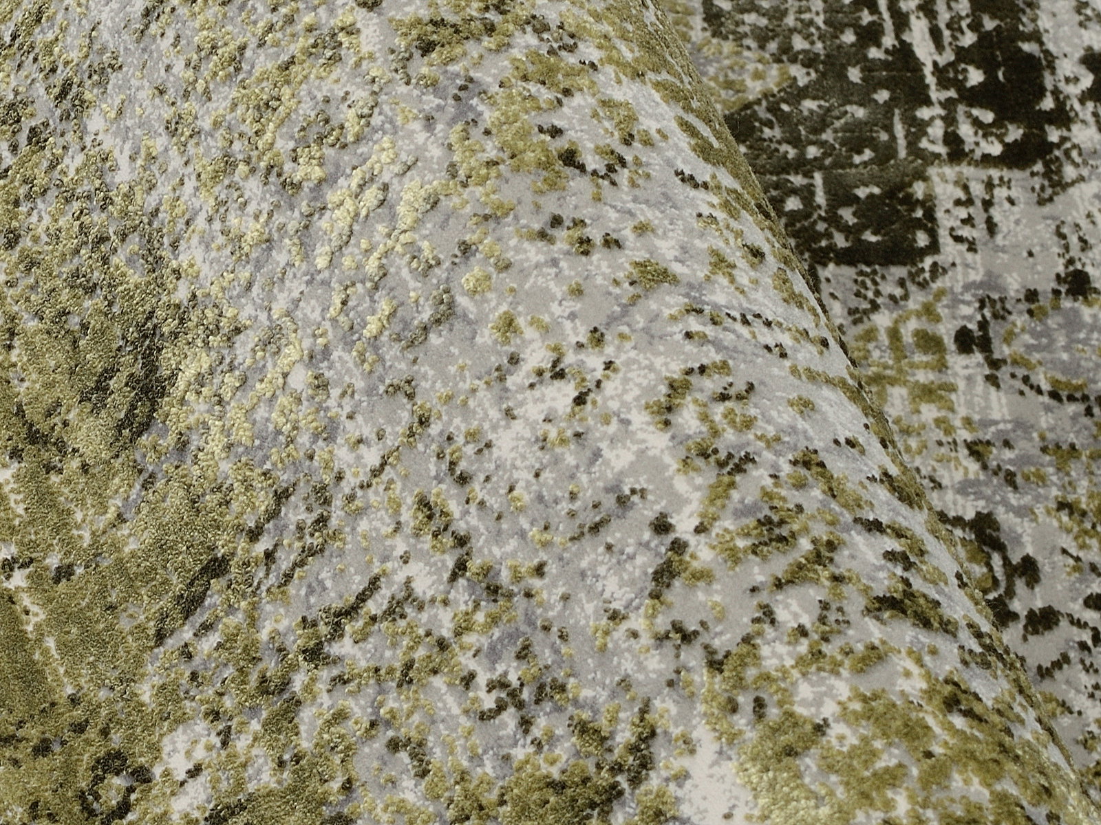 Nahaufnahme eines Designer-Teppichs mit abstraktem Muster in Grün- und Grautönen, perspektivisch von der Seite aufgenommen.