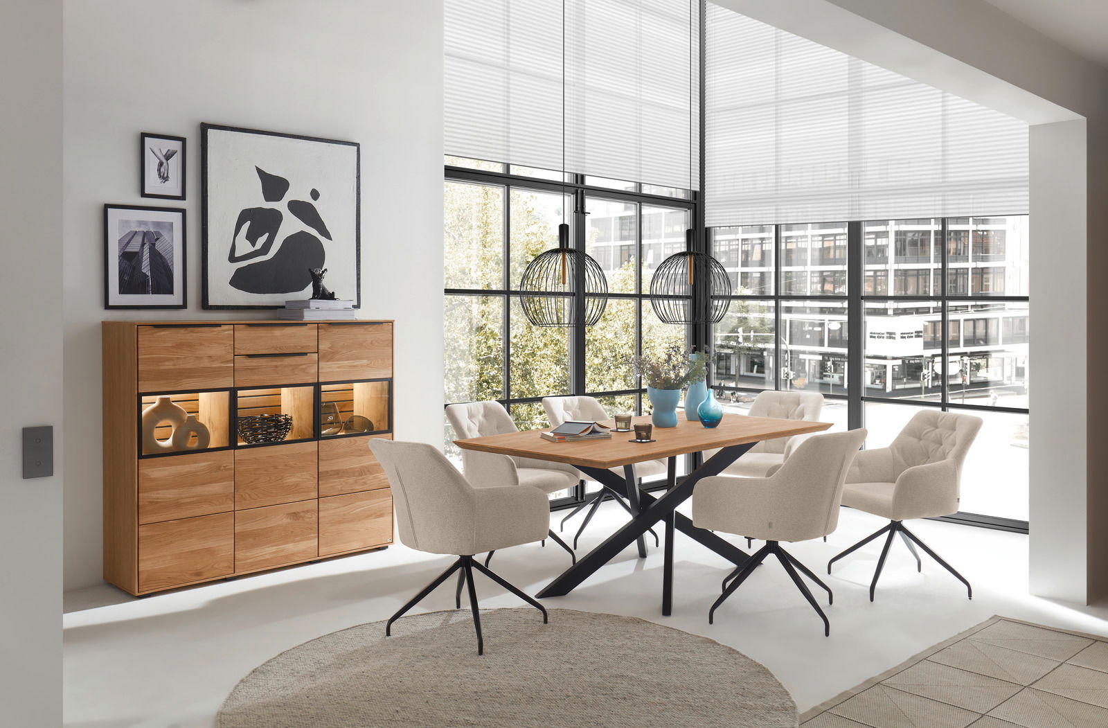 Moderne Esszimmer-Einrichtung mit einem Holztisch und beigen Stühlen, im Hintergrund ein Highboard mit Dekorationen, seitliche Perspektive.