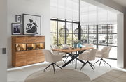 Moderne Esszimmer-Einrichtung mit einem Holztisch und beigen Stühlen, im Hintergrund ein Highboard mit Dekorationen, seitliche Perspektive.