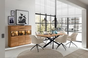 Moderne Esszimmer-Einrichtung mit einem Holztisch und beigen Stühlen, im Hintergrund ein Highboard mit Dekorationen, seitliche Perspektive.