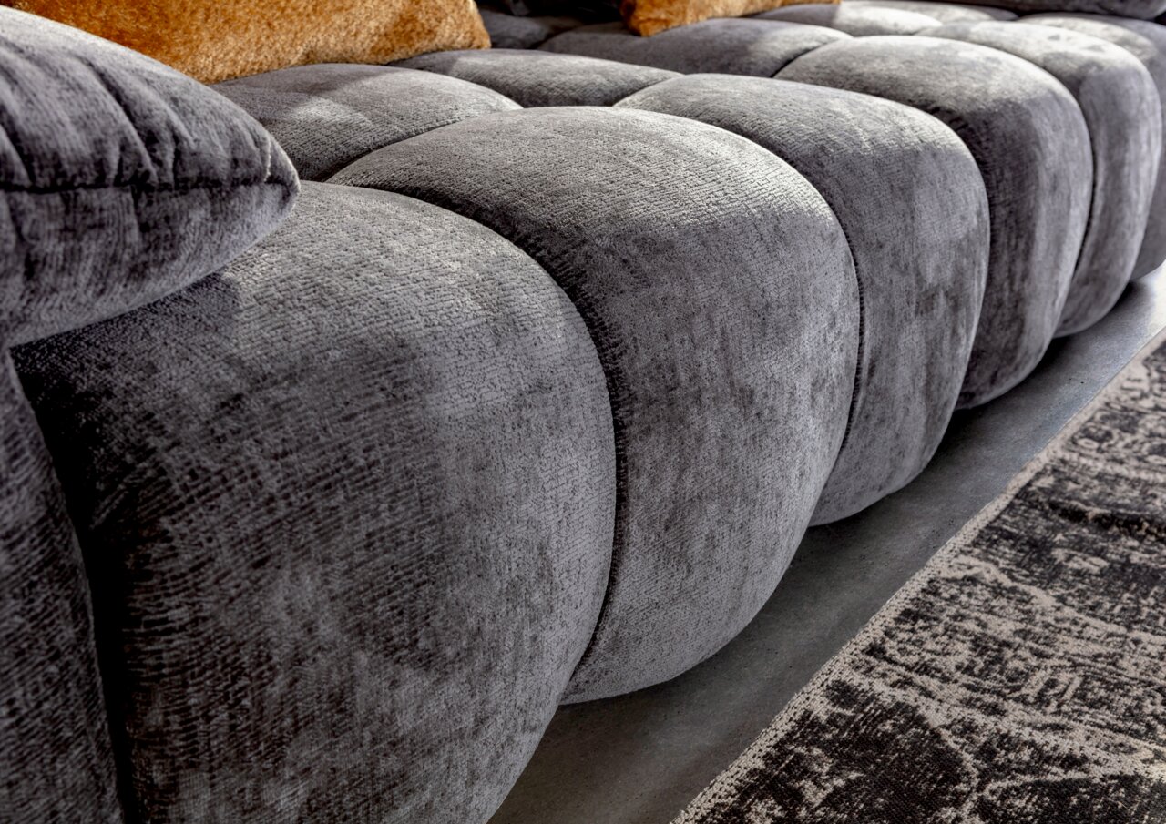 Nahaufnahme eines grauen Megasofas mit weicher, gepolsterter Oberfläche und seitlicher Perspektive.