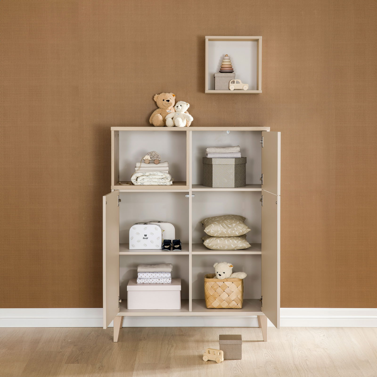 Highboard mit offenen und geschlossenen Fächern, gefüllt mit Spielzeug und Textilien, aus frontaler Perspektive.