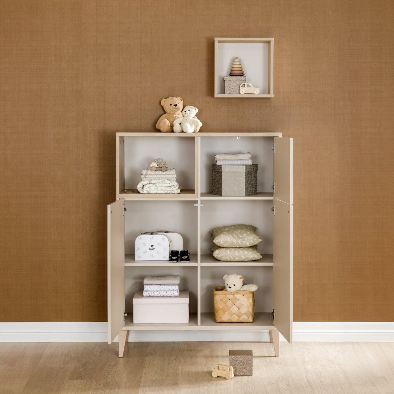 Highboard mit offenen und geschlossenen Fächern, gefüllt mit Spielzeug und Textilien, aus frontaler Perspektive.