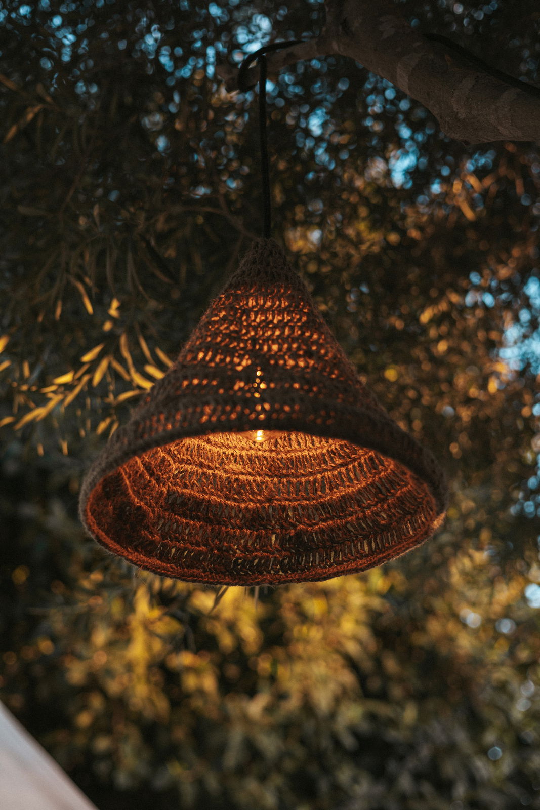 Outdoor-Hängeleuchte aus geflochtenem Material, beleuchtet in einem Baum hängend, seitliche Perspektive