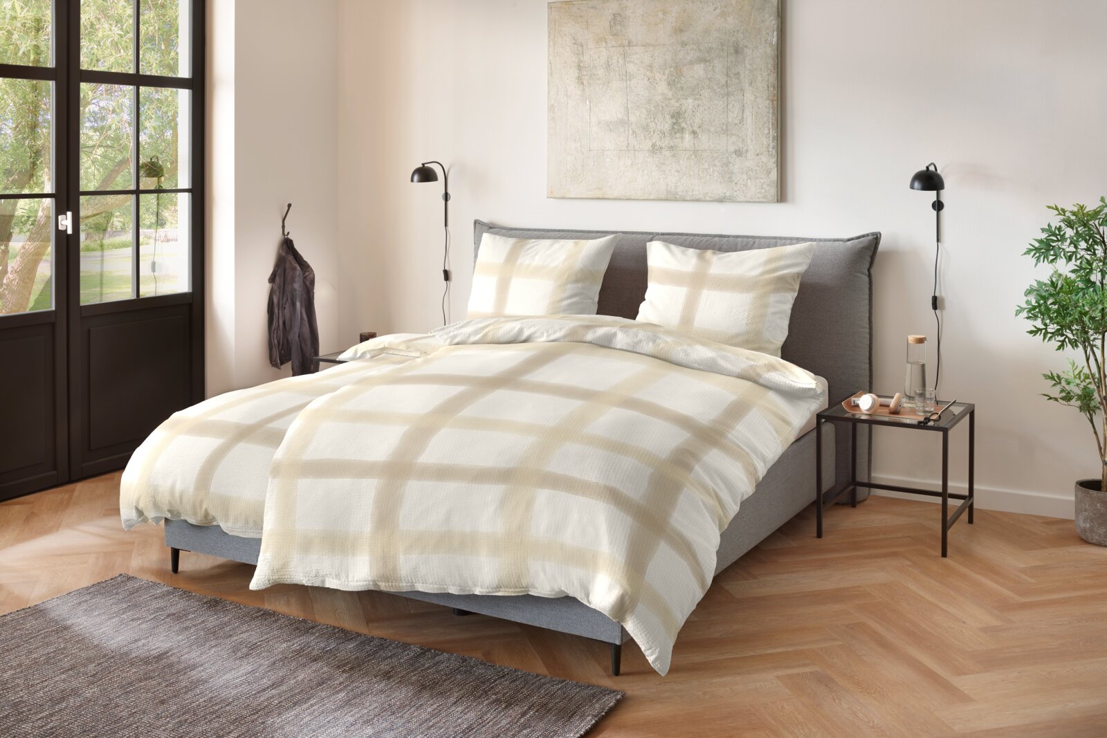 Primera Soft-Seersucker Bettwäsche 135/200cm Modernes Schlafzimmer mit grauem Polsterbett und Bettwäsche in Weiß mit beigefarbenem Karomuster, aufgenommen aus leicht erhöhter Frontansicht.