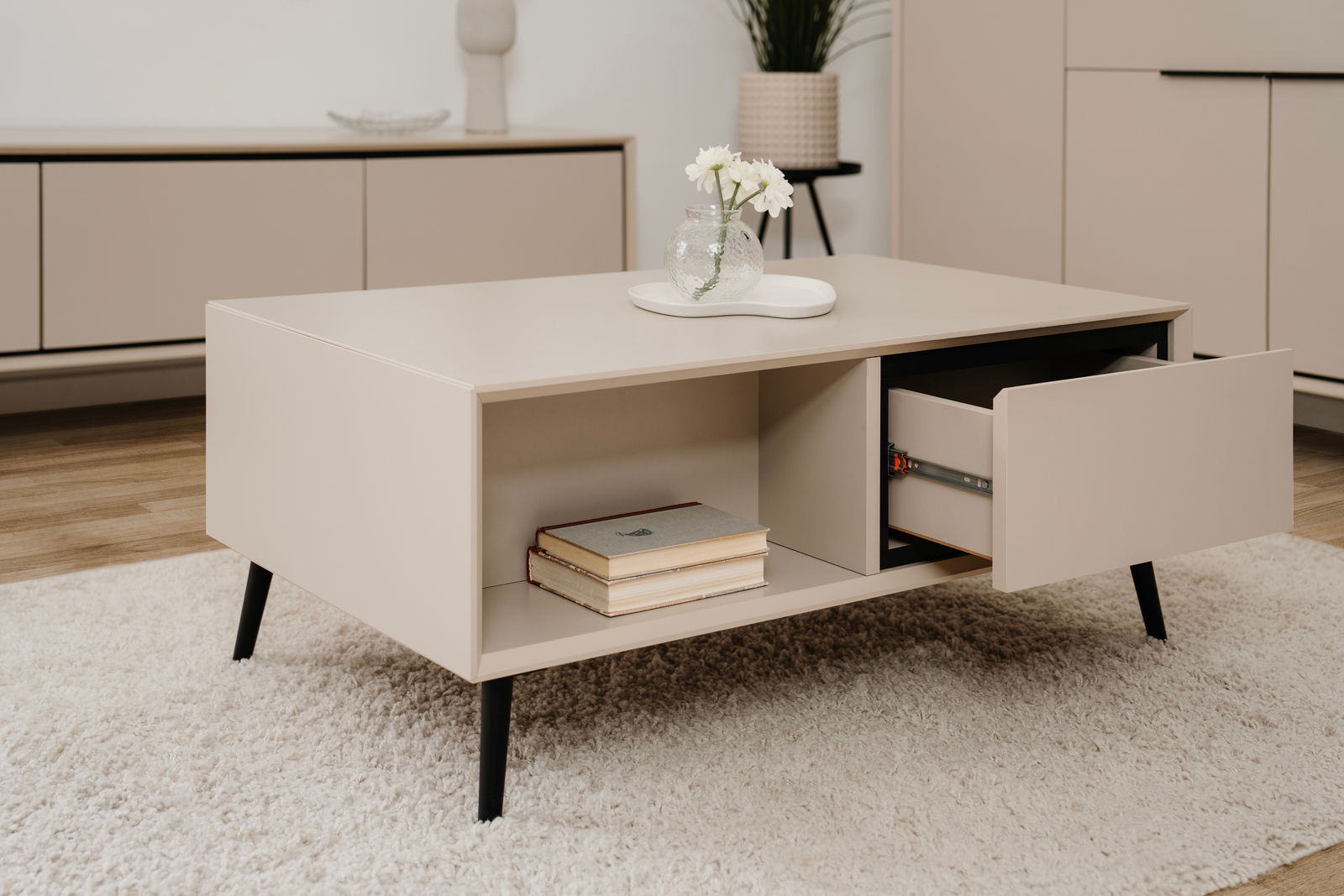 Beige Sideboard mit schwarzem Bein, offene Schublade und Bücher, aus seitlicher Perspektive fotografiert.