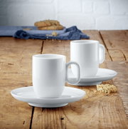 Zwei weiße Espressotassen mit Untertassen aus dem WMF Barista Espresso Tassen-Set auf einem Holztisch, seitliche Perspektive.