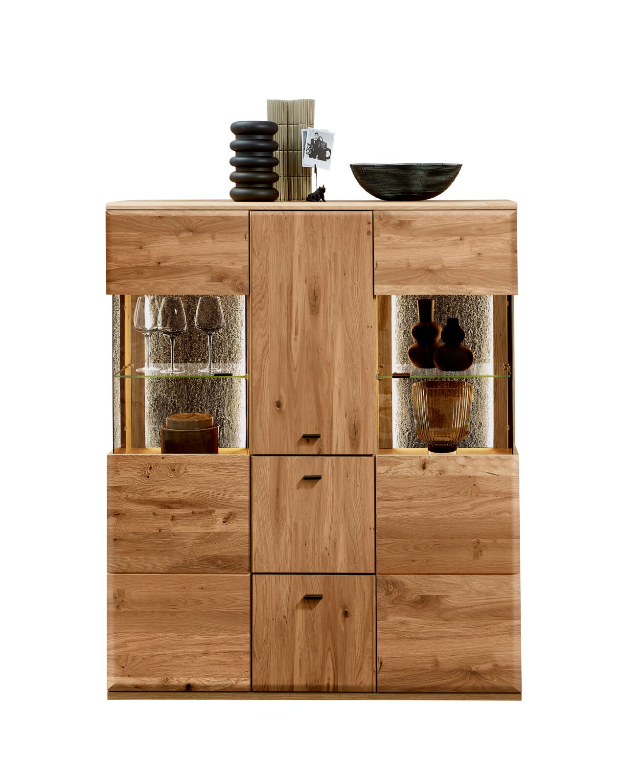 Frontansicht eines modernen Highboards aus massivem, naturfarbenem Holz mit zwei beleuchteten Glasvitrinen links und rechts sowie mittigen Schranktüren, dekoriert mit Vase, Büchern und Schale auf weißem Hintergrund