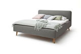 Graues Polsterbett mit Holzfüßen, dekoriert mit Kissen und einer Decke, seitliche Perspektive