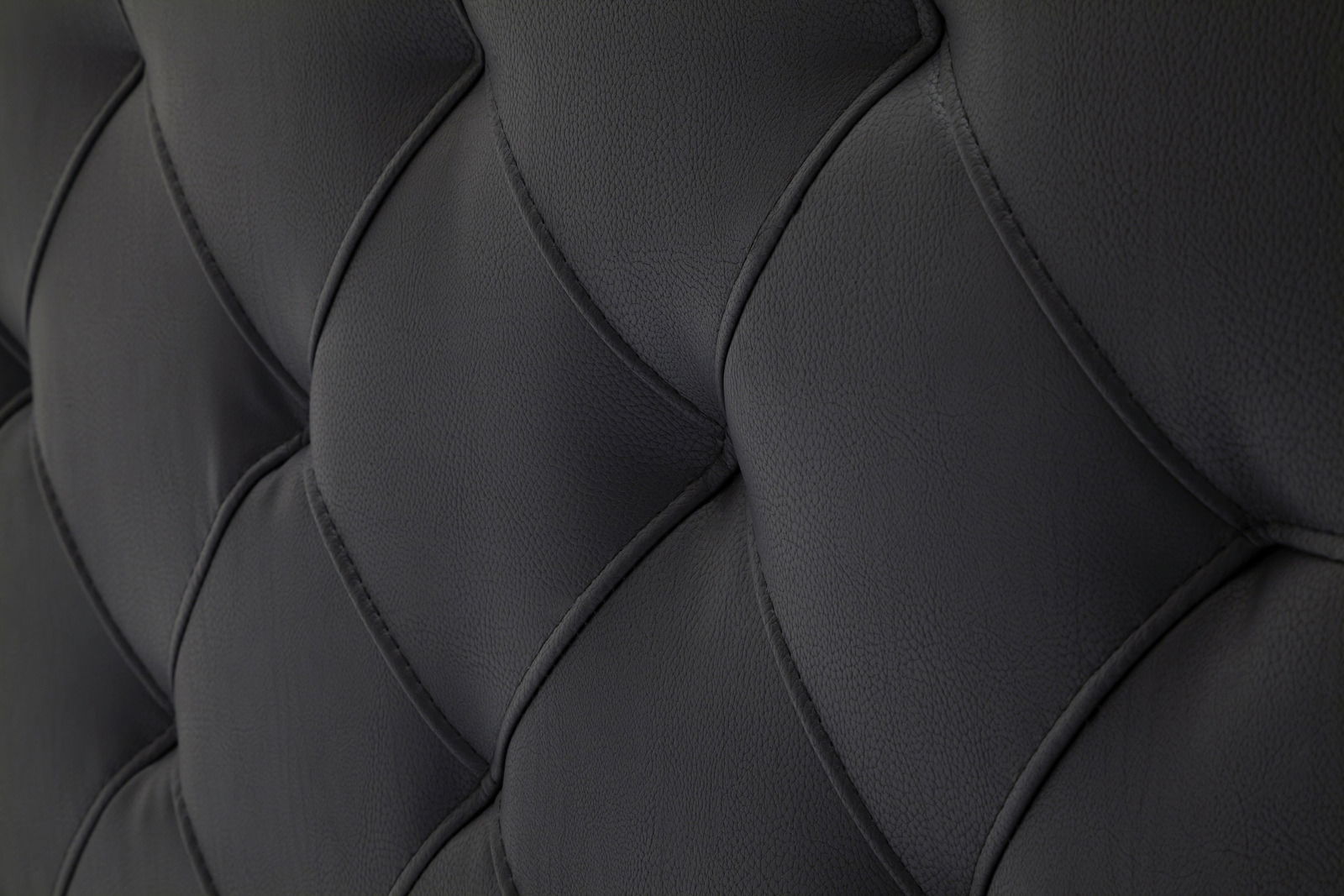 Nahaufnahme des gepolsterten Kopfteils eines Polsterbetts in dunklem Leder mit gestepptem Muster.