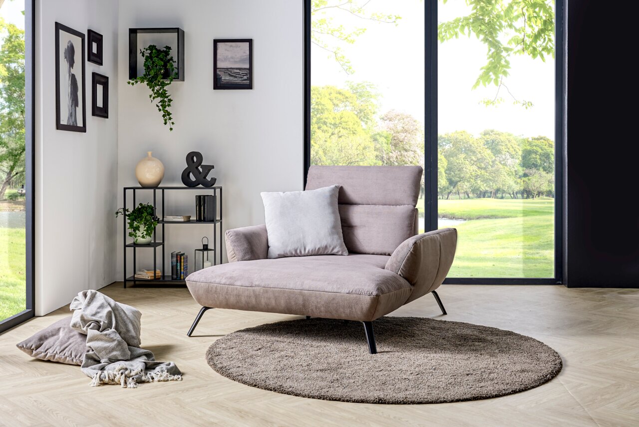 Modernes Loveseat in einem hellen Raum mit großen Fenstern, umgeben von stilvoller Dekoration. Perspektive von vorne links.