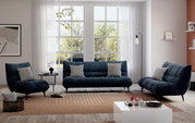 Modernes Wohnzimmer mit einem blauen 3-sitzigen Sofa, flankiert von zwei passenden Sesseln, in einer hellen Umgebung mit großen Fenstern und minimalistischer Dekoration. Frontalansicht.