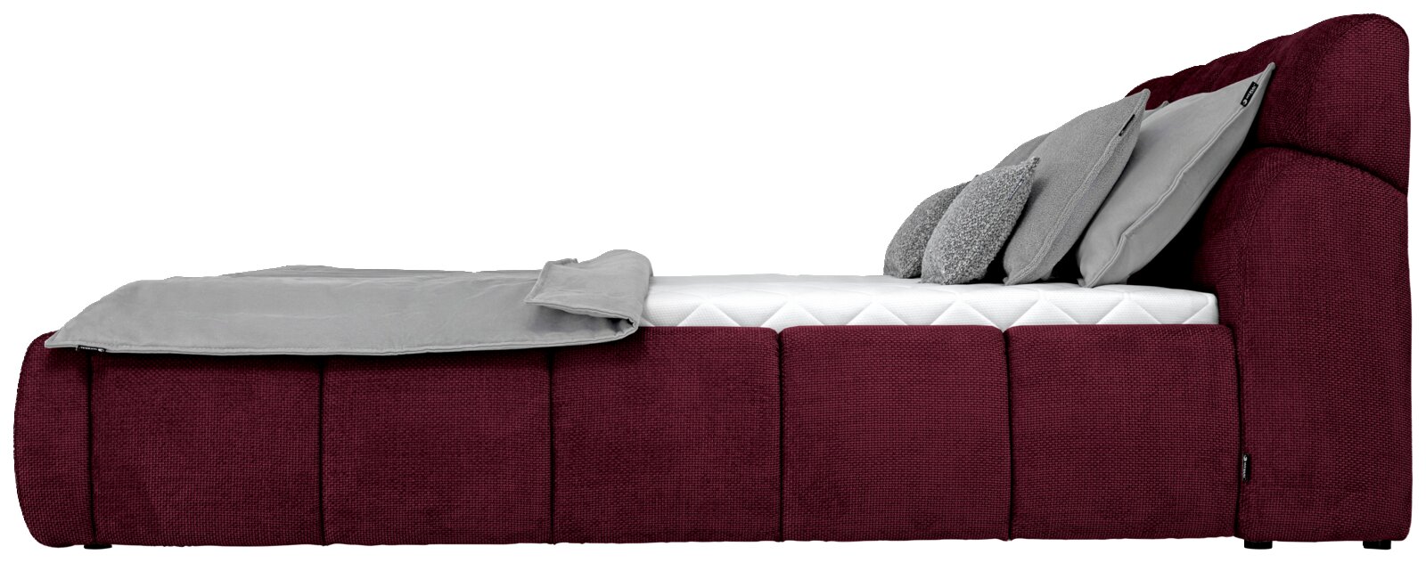 Zijaanzicht van een gestoffeerd bed in de kleur Bordeaux met grijze kussens en een deken.