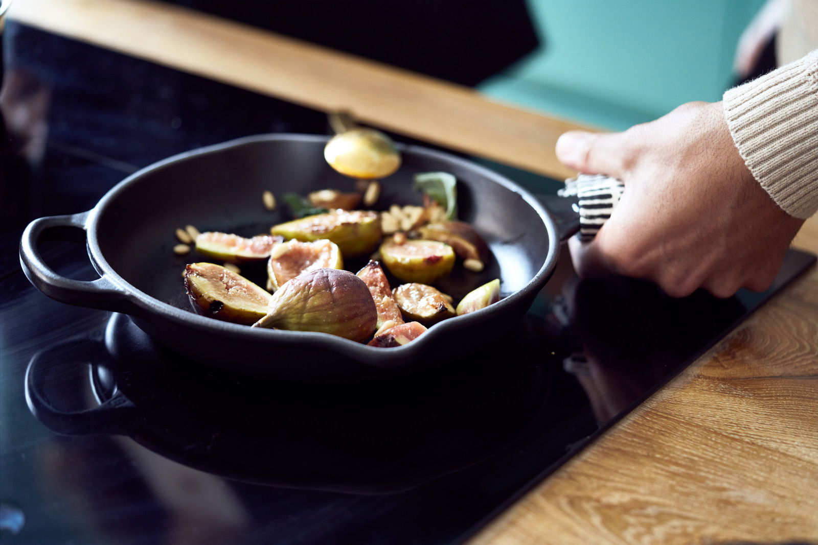 Nahaufnahme einer Brat- und Servierpfanne mit Griffen, in der auf einem Herd frische Feigen zubereitet werden.