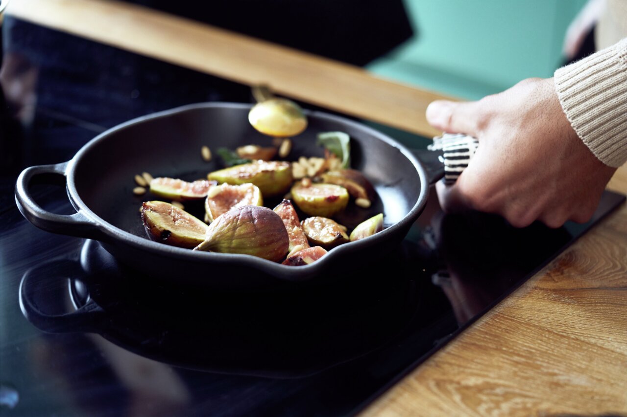 Nahaufnahme einer Brat- und Servierpfanne mit Griffen, in der auf einem Herd frische Feigen zubereitet werden.