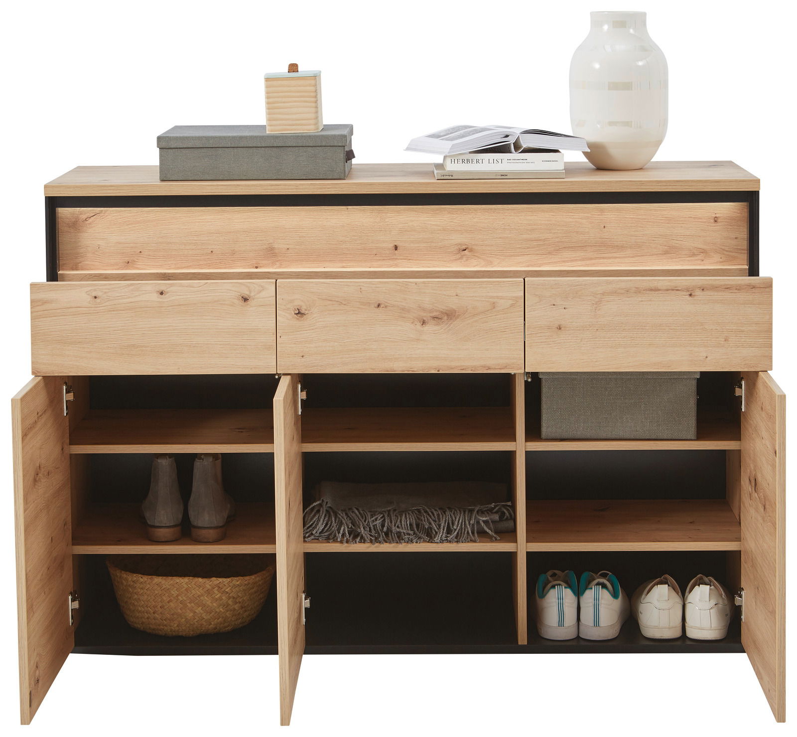 Frontale Ansicht eines modernen Sideboards mit Holzoptik, offenen Schubladen und Türen, gefüllt mit Schuhen, Körben und Dekorationen.