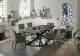 Moderner Esstisch mit schwarzer Tischplatte und X-förmigem Gestell, umgeben von grünen Stühlen in einem stilvoll eingerichteten Esszimmer, seitliche Perspektive.